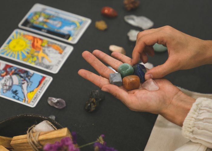 Person holding healing crystals with tarot cards in the background, symbolizing spirituality.